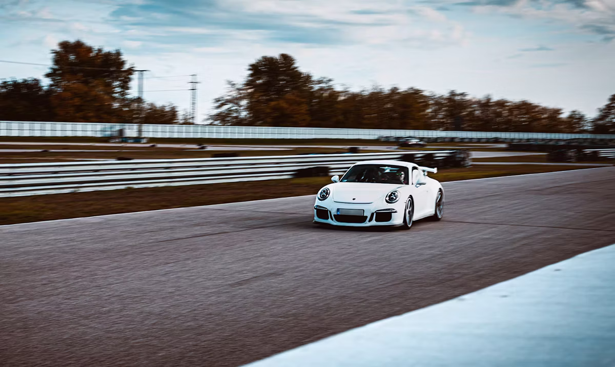 A white Porsche 911 on track with fall trees behind