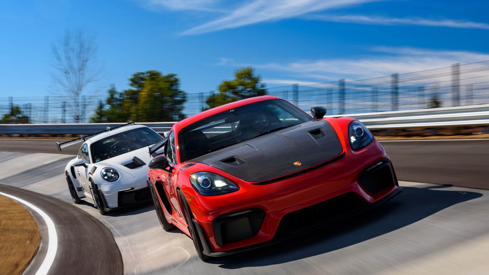 A red Porsche 718 leading a white 911 through a corner at Porsche Experience Center Atlanta
