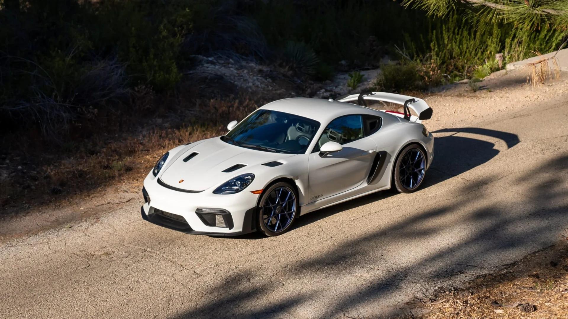 A white Porsche 718 on a sunlit road
